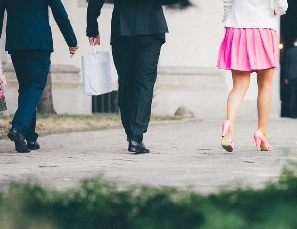 Three lawyers walking away. One lawyer stands out from the suits, in a pink skirt.